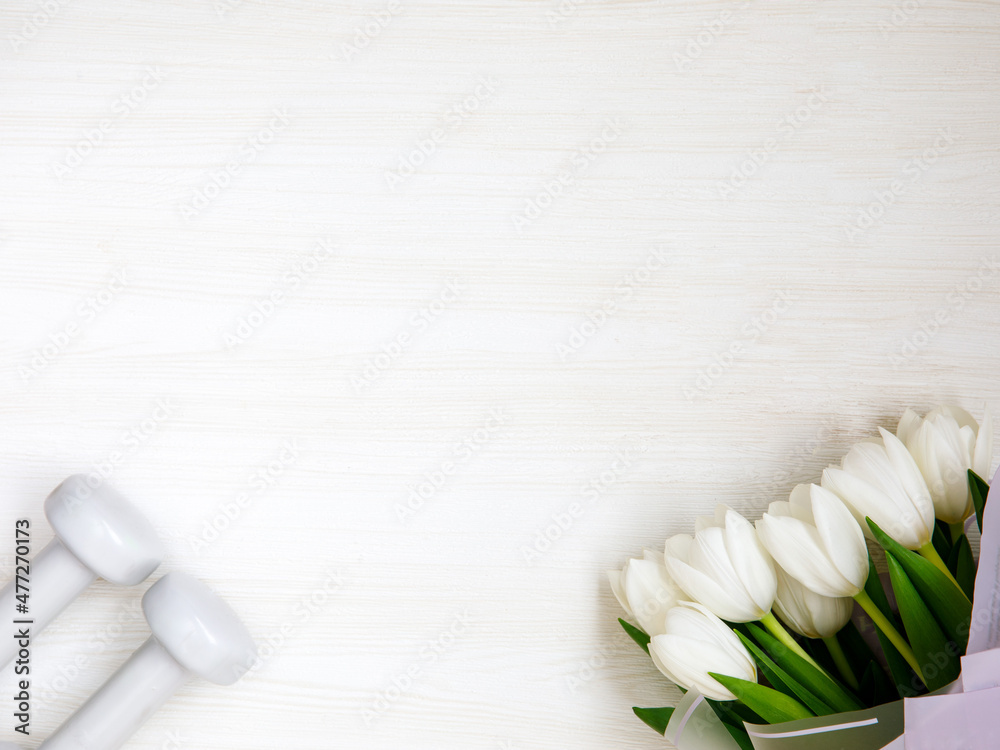 Two white dumbbells and tulips on white background with copyspace. Healthy fitness lifestyle flat lay composition for Valentine's Day, birthday, anniversary or wedding.