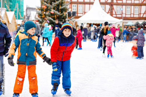 Two happy kids boys in colorful warm clothes skating on a rink of Christmas market or fair. Healthy children, siblings and best friends having fun on ice skate. People having active winter leisure