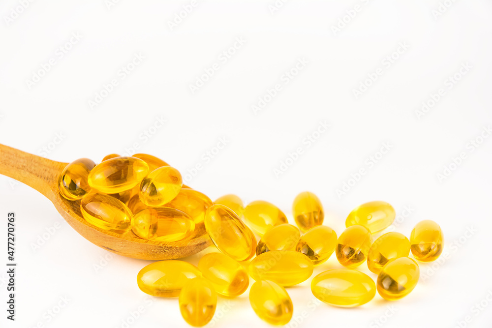 Fototapeta premium Yellow oil soft gel capsules in wooden spoon on white background