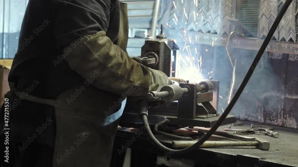 Welding of metal parts in a factory. A man in a protective suit connects the parts using semi-automatic welding. Production of metal structures Welding of metal parts in a factory. A man in a protective suit connects the parts using semi-automatic welding. Production of metal structures