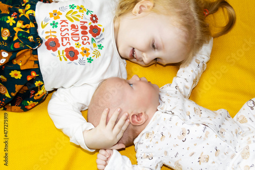 The older sister looks after and plays with her newborn brother on the sofa and a yellow background.