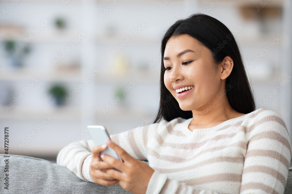 Smiling Young Asian Woman Browsing Internet On Smartphone While Resting At Home Smiling Young Asian Woman Browsing Internet On Smartphone While Resting At Home