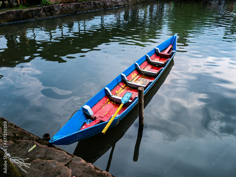 a small blue-red boat that floats in a small reservoir
