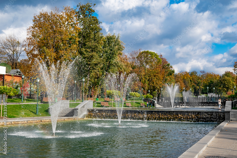 Kharkiv, Ukraine - October 20, 2020: Fountains in the autumn Shevchenko garden in Kharkov. Pond with jets of water gushing upwards against the background of golden trees in a city park