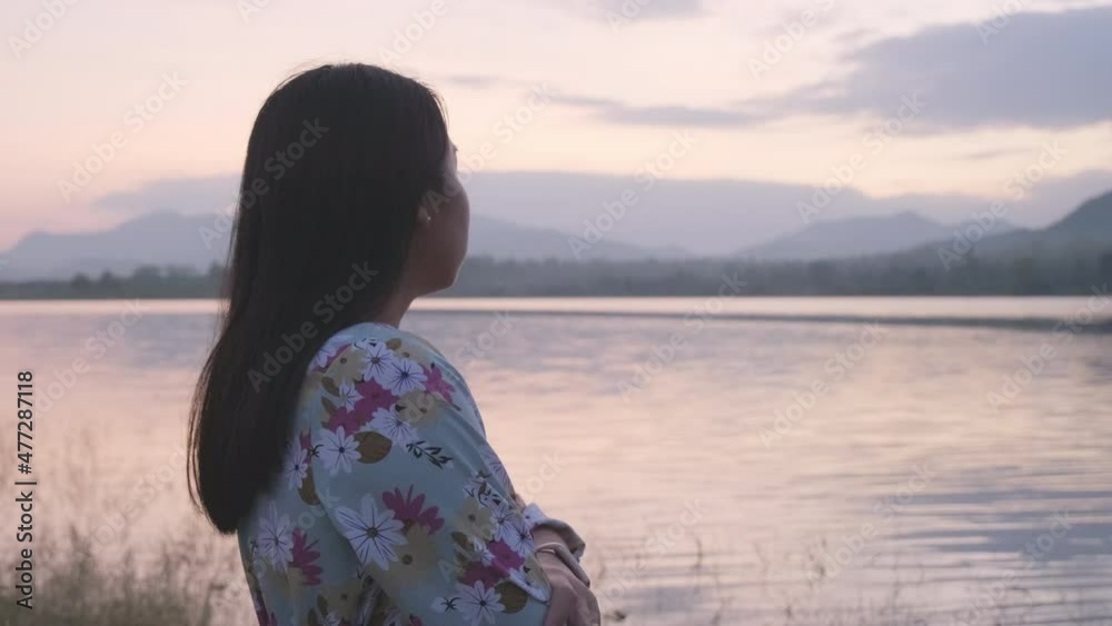 Young asian woman crossing arms with feeling alone by the lake in winter at sunset. Side view of lonely woman relaxing breathing fresh air outdoors in winter at lakeside. Young asian woman crossing arms with feeling alone by the lake in winter at sunset. Side view of lonely woman relaxing breathing fresh air outdoors in winter at lakeside.