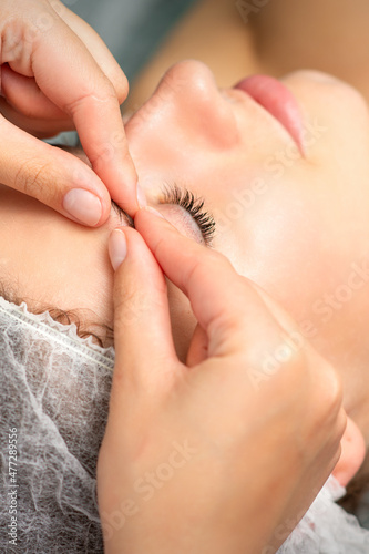 Manual sculpting face massage in the spa. Fingers of beautician make facial massage eyebrow of a young woman in cosmetology clinic, close up