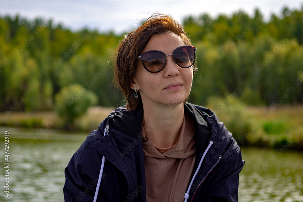 Young woman in sunglasses on the background of the surface of a forest lake. Warm autumn day