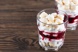 Dessert with aquafaba meringue, coconut cream and cherries in a glass on a wooden table. Sugar, lactose free, vegan. Horizontal orientation, copy space.