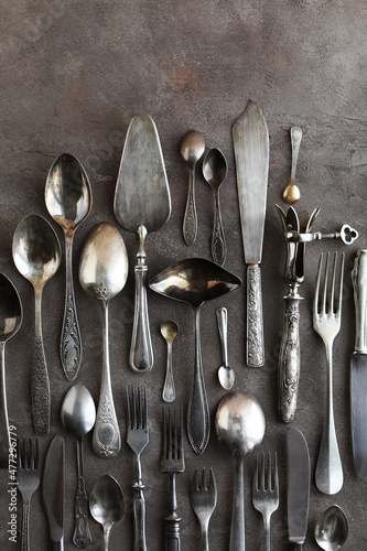 Lots of vintage cutlery sets on a gray and beige table. Vintage spoons, forks and knives on a solid background