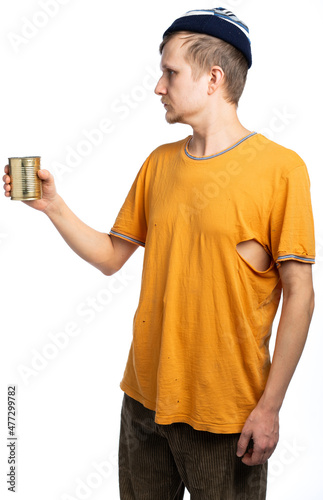 Fotografie, Obraz a homeless man looks away, holds a can of canned food, an orange torn T-shirt
