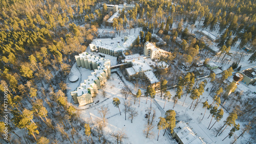 Aerial view of the postmodern sanatorium building surrounded by forest. Winter sunny day. Flying by drone