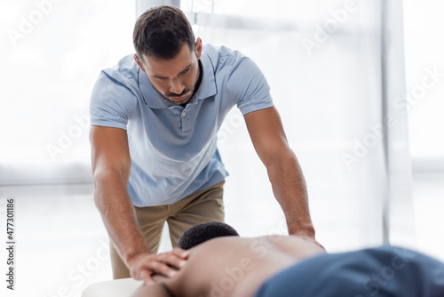 masseur doing back massage to blurred african american man in rehabilitation center