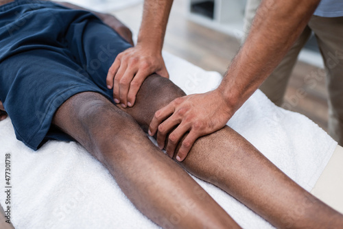 cropped view of masseur massaging knee of african american man in rehab center