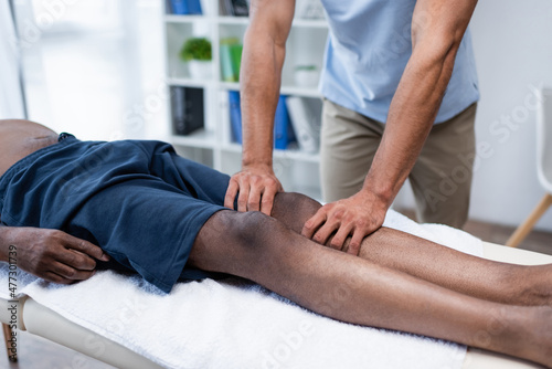 partial view of rehabilitologist massaging leg of african american man