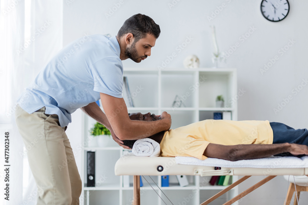 Obraz premium side view of young physiotherapist treating african american patient in rehab center