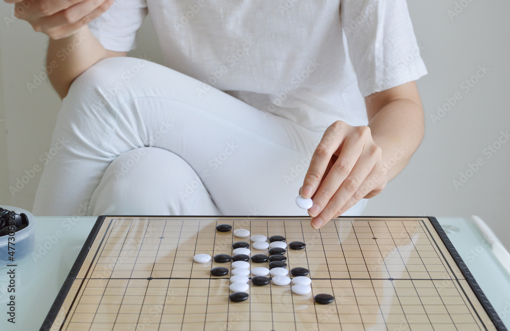 Straight view of GO board game table with woman hand holding a stone Straight view of GO board game table with woman hand holding a stone