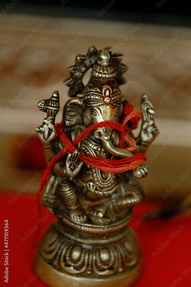 Fototapeta premium The Hindu god Ganesha statue Idol of Hindu god Ganesh covered with red thread stands on the table at the Indian wedding Indian Wedding Ceremony Cropped photo Close up