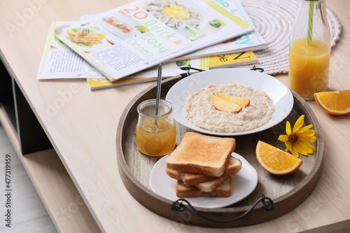 Wooden tray with delicious breakfast and beautiful flower on table