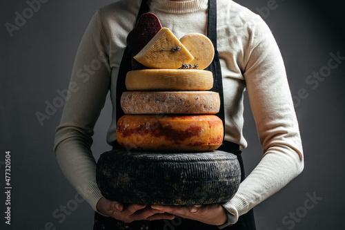 A head of hard cheese in woman's cheesemaker hands. Different delicious dairy products