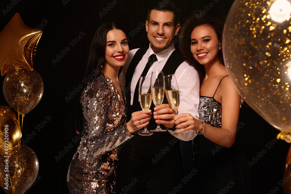 Happy friends with glasses of sparkling wine celebrating New Year on black background