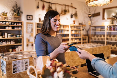 Pregnant female paying with smartphone in eco friendly store photo