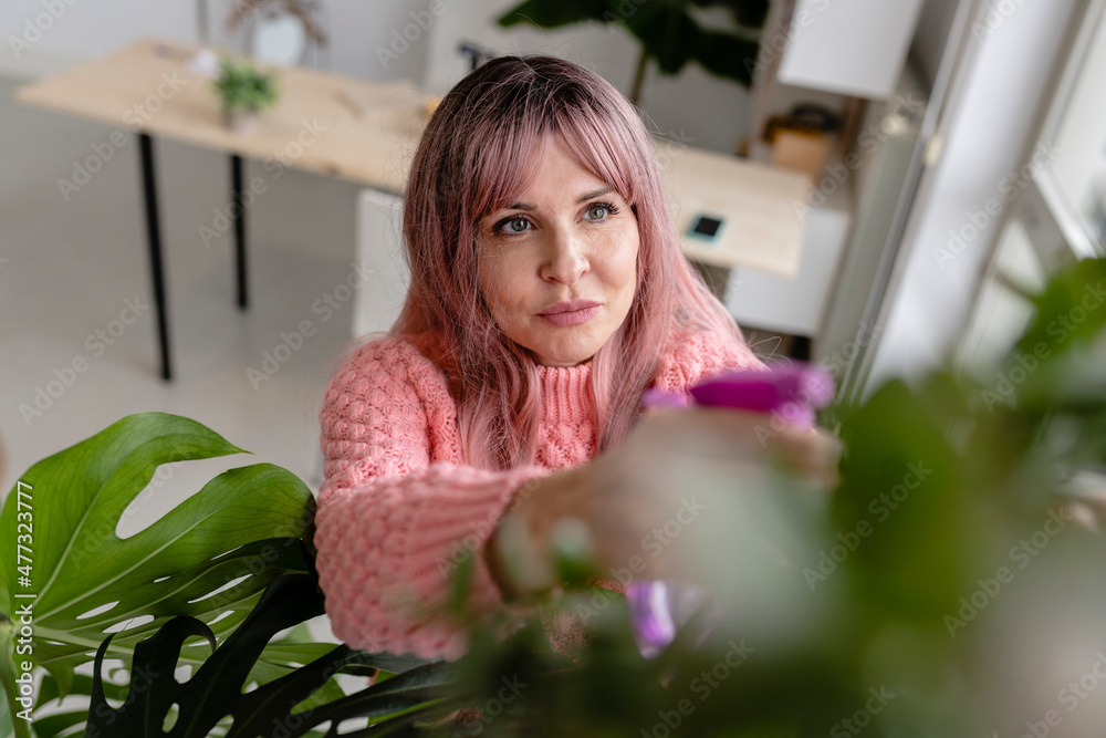 Woman spraying leaves in apartment