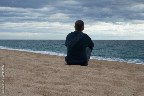 Adult man sitting on the beach pensively contemplating the sea