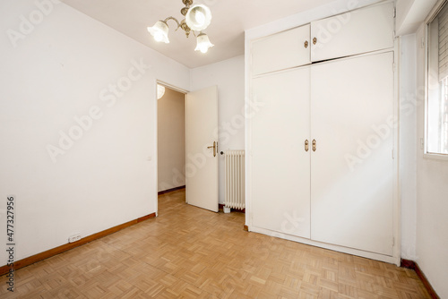 Empty room with white walls and oak parquet floors and fitted wardrobe with white doors