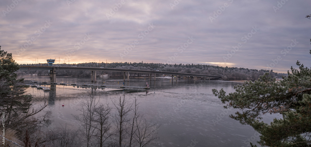 Panorama view with a bridge at the lake Mälaren, view from a cliff with forest sky line and an icy bay a winter afternoon day in Stockholm