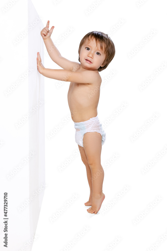 Portrait of little boy, baby, child in diaper standing near wall isolated over white studio background. Childhood concept