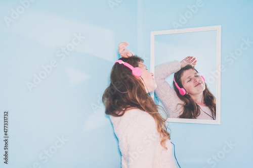 Smiling woman with eyes closed listening music through headphones in front of mirror at home
