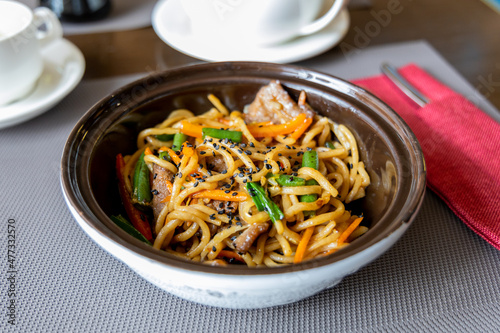 Noodles with beef and vegetables in teriyaki sauce. Beans, sesame seeds. Noodles, a ready-made dish in a restaurant. Grey tablecloth. Lunch at the restaurant
