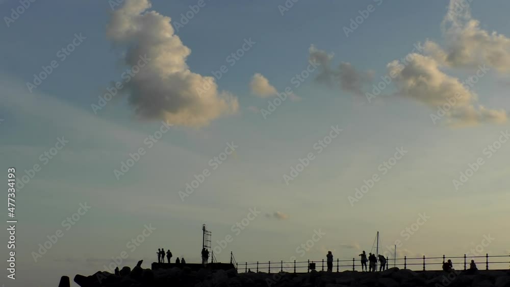 Silhouettes of holidaying people on pier and large stones against sunset sky, plenty of copy space. Silhouettes of holidaying people on pier and large stones against sunset sky, plenty of copy space.