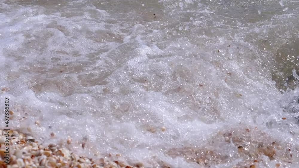 Sea Wave with Foams Rolls onto the Sandy Shore from Shells. Splashes, sprays of seawater. Multi-colored seashells. Shell rock. Stormy weather on the coast of the Sea of Azov. Beach vacation concept. Sea Wave with Foams Rolls onto the Sandy Shore from Shells. Splashes, sprays of seawater. Multi-colored seashells. Shell rock. Stormy weather on the coast of the Sea of Azov. Beach vacation concept.