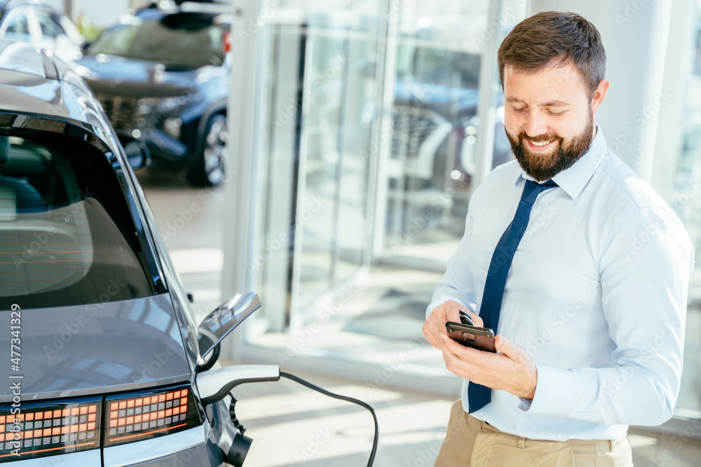 Handsome business man charging his electric car at charge station and using smartphone. Handsome business man charging his electric car at charge station and using smartphone.