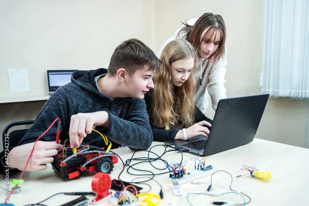 Diverse teenager pupils build robot vehicle learning at table at STEM engineering science education class. School students making robotic cars using laptop computer. - obrazy, fototapety, plakaty 
