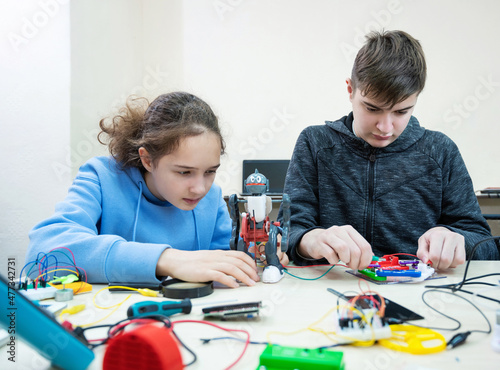 Teenager boy and girl at robotics school makes robot managed from the constructor, child learns robot constructing.