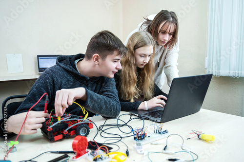 Diverse teenager pupils build robot vehicle learning at table at STEM engineering science education class. School students making robotic cars using laptop computer. photo