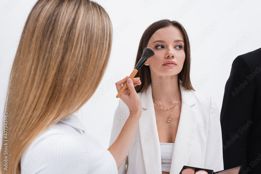 blonde makeup artist applying makeup on young brunette model isolated on white. blonde makeup artist applying makeup on young brunette model isolated on white.