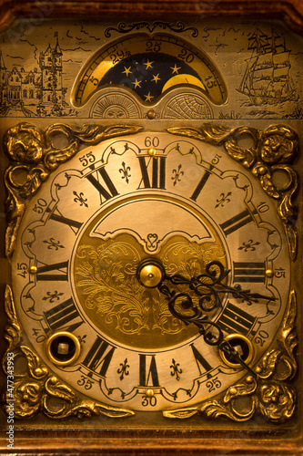 Closeup of the dial of an old wind-up table clock made in The Netherlands. Highly decorated vintage wooden clock with moon dial.