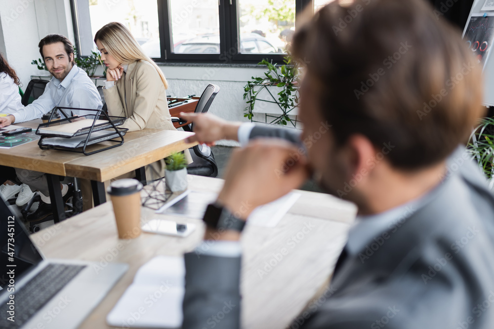 blurred businessman pointing at young colleagues working in office. blurred businessman pointing at young colleagues working in office.