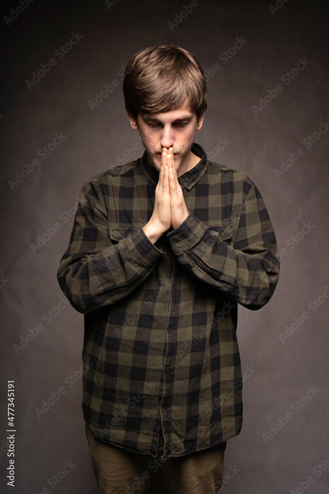 Young handsome tall slim white man with brown hair praying with flannel shirt on grey background Young handsome tall slim white man with brown hair praying with flannel shirt on grey background
