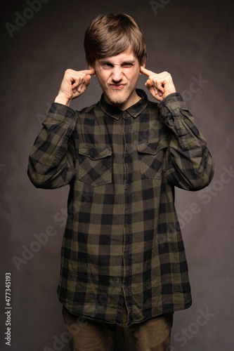 Young handsome tall slim white man with brown hair covering his ears with flannel shirt on grey background