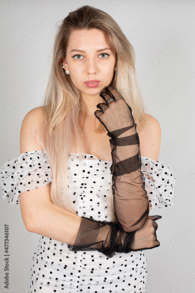 Young woman with blond hair and white skin isolated on grey in white dress in dots Young woman with blond hair and white skin isolated on grey in white dress in dots
