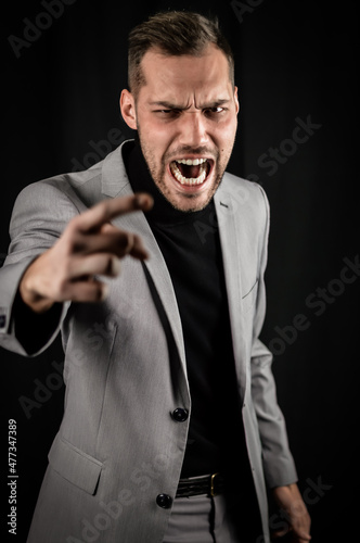 portrait of a young businessman in a gray suit, very angry yelling and gesturing accusingly in front of him