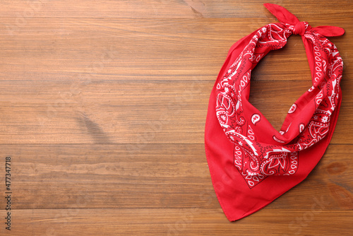 Tied red bandana with paisley pattern on wooden table, top view. Space for text