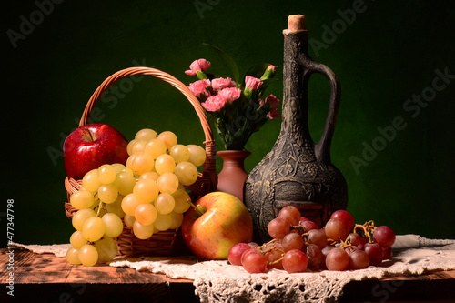 Obraz z winem w tle. Martwa natura a w niej świeże owoce takie jak winogron czerwona, biała, jabłka, mandarynki klementynki oraz limonka z bukietem goździków. kompozycja na pulpit czy obraz na ścianę