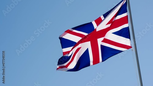 British Flag and Blue Sky. The Big State Flag is illuminated by the sun and flutters epically in the wind against the blue sky. Slow Motion 120 fps photo