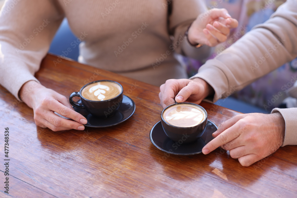 Couple with cups of aromatic coffee at wooden table, closeup