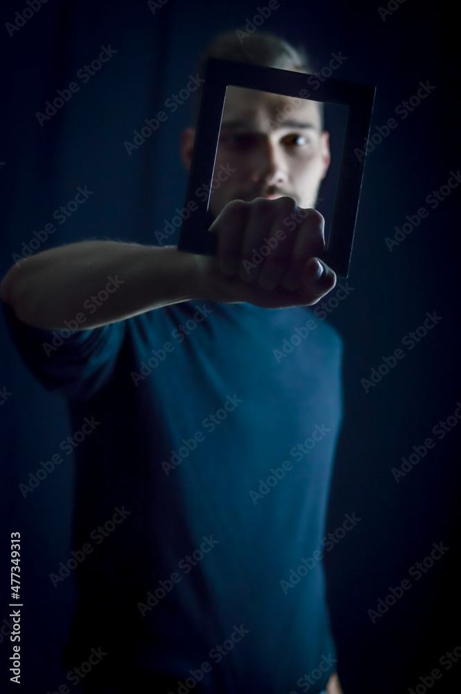 portrait of a young man holding a frame in front of his face, concept for the uniqueness of individuals, focus on the hand 